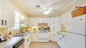 A kitchen with white cabinets, a stove, a refrigerator, and a ceiling fan.