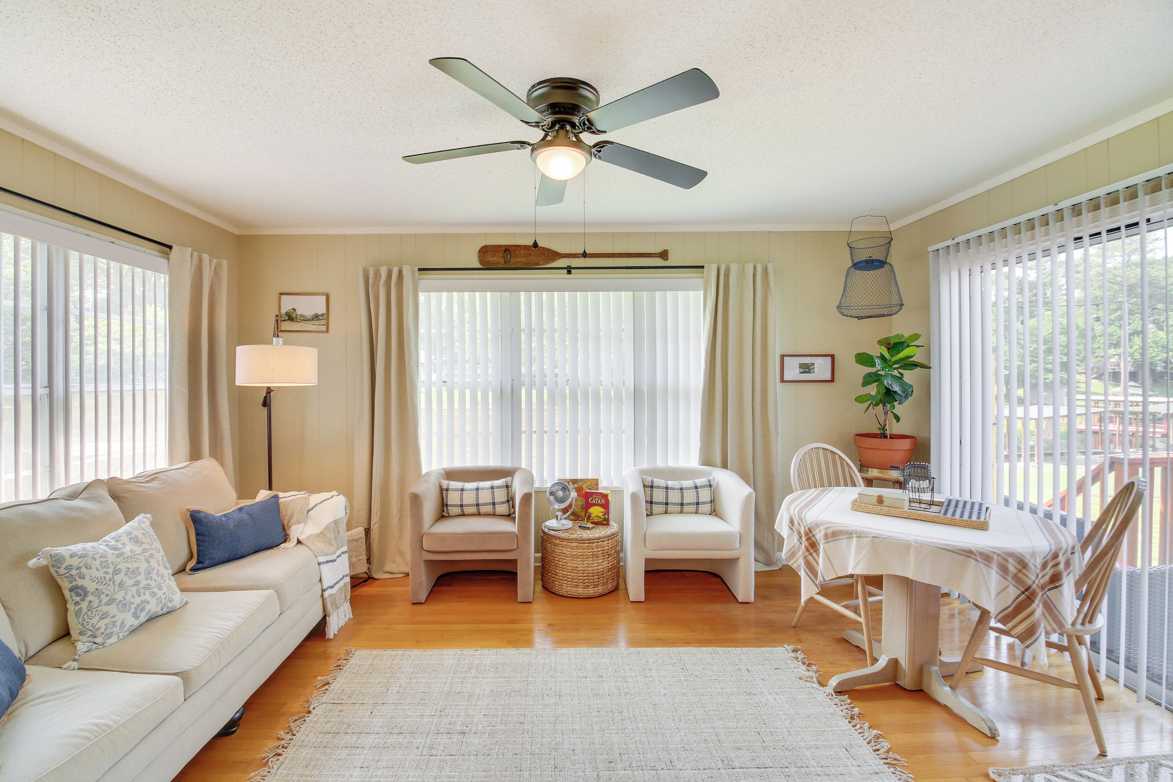 A living room with a sofa, two armchairs, a small table, a ceiling fan, and a window with blinds.
