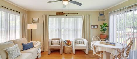A living room with a sofa, two armchairs, a small table, a ceiling fan, and a window with blinds.