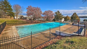 A rectangular swimming pool with a black metal fence, surrounded by grass and trees, with a clear blue sky above. - Cozy Hot Springs Vacation Rental on Lake Hamilton! (Hot Springs)