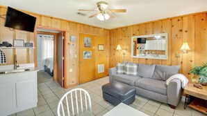 A cozy room with a kitchenette, a gray sofa, a white chair, and a ceiling fan. - Cozy Hot Springs Vacation Rental on Lake Hamilton! (Hot Springs)