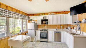 A kitchen with white cabinets, a stove, a refrigerator, and a sink. There is a window with a view of trees and a sign that says "BE HAPPY". - Cozy Hot Springs Vacation Rental on Lake Hamilton! (Hot Springs)
