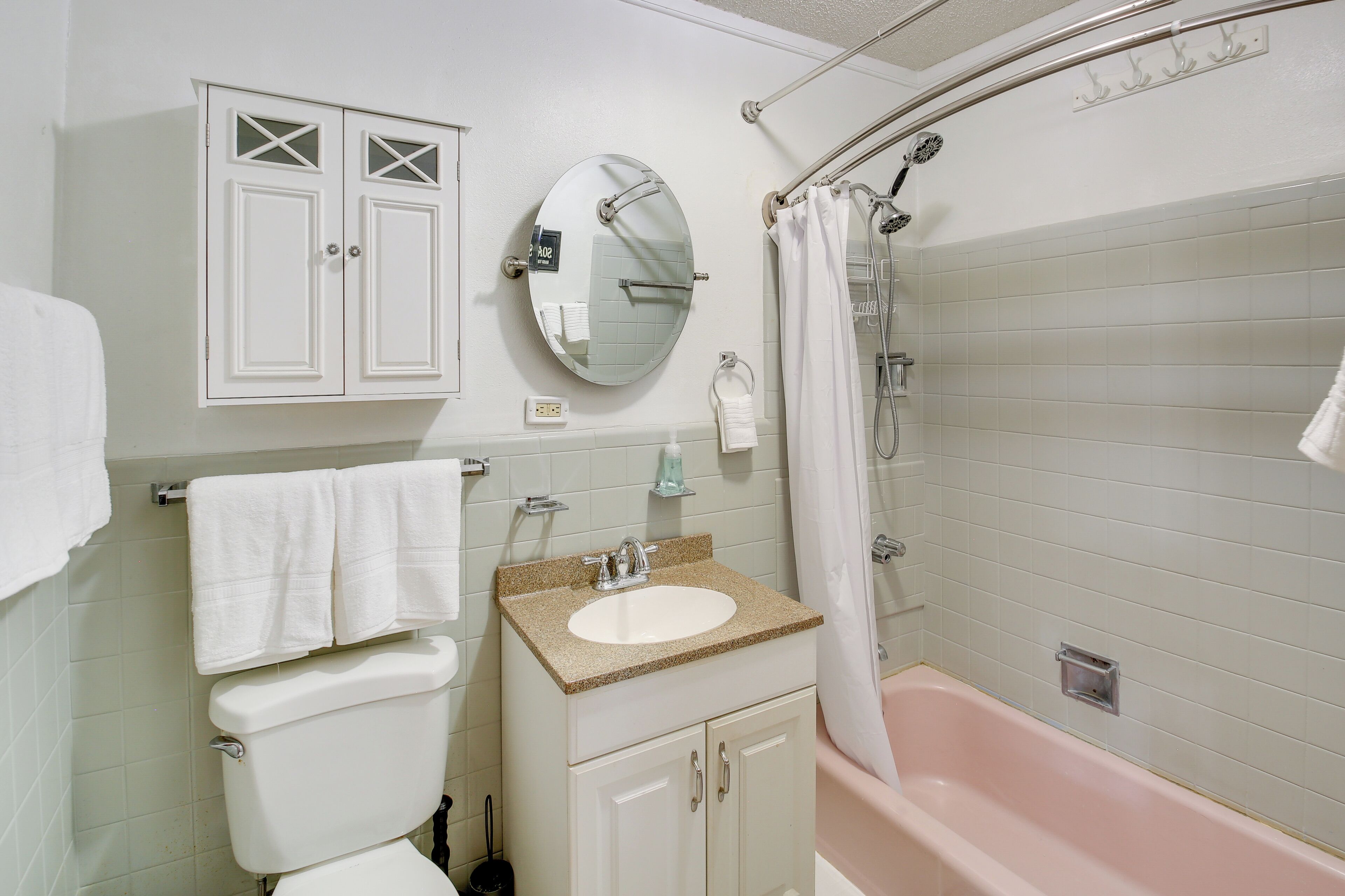 A bathroom with a toilet, sink, mirror, and bathtub.
