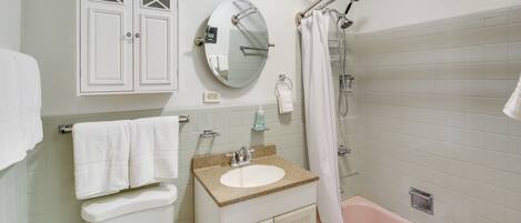 A bathroom with a toilet, sink, mirror, and bathtub.