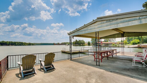 A lakeside patio with Adirondack chairs, a picnic table, and a covered seating area. - Cozy Hot Springs Vacation Rental on Lake Hamilton! (Hot Springs)