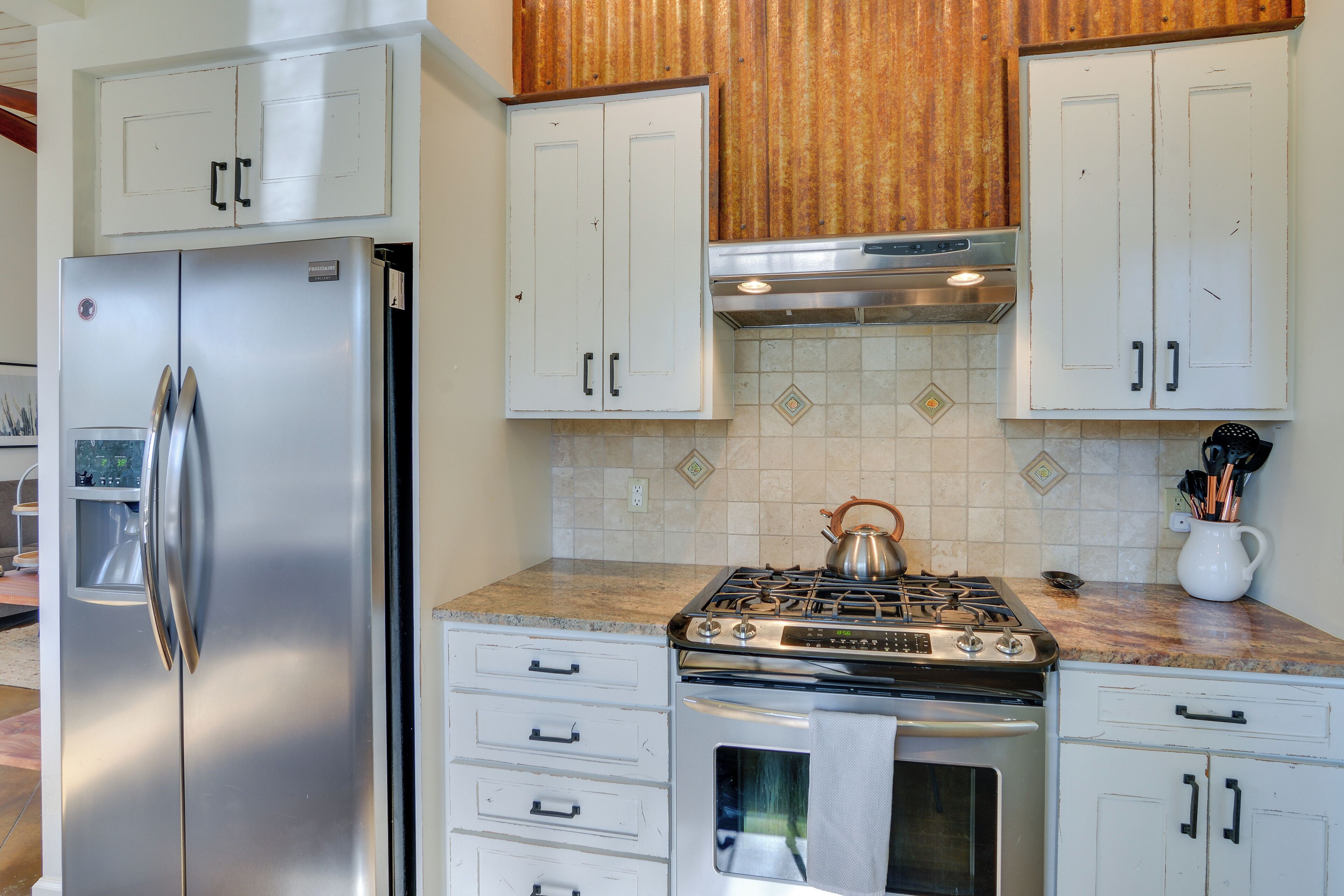 A kitchen with stainless steel appliances, white cabinetry, and a tiled backsplash.