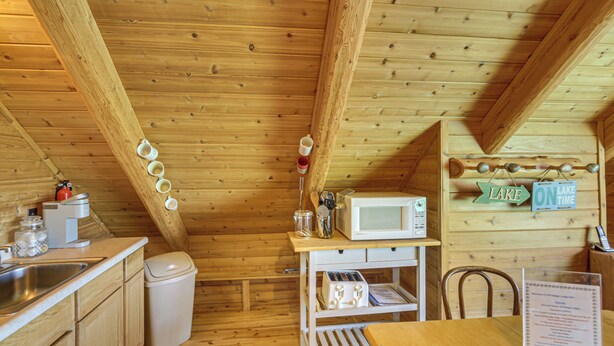 A wooden cabin interior with a kitchen area, including a sink, microwave, and wooden cabinets. - Waterfront 'UP Badger Lodge Bnb' on Powell Lake (Wetmore)