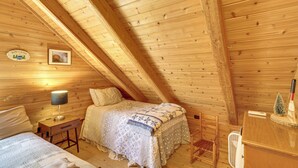A cozy attic bedroom with a wooden ceiling, a bed with a patterned bedspread, a bedside table with a lamp, and a small fan. - Waterfront 'UP Badger Lodge Bnb' on Powell Lake (Wetmore)