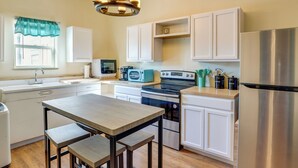 A modern kitchen with white cabinets, a stainless steel refrigerator, a microwave, and a stove. There is a wooden table with two stools and a window with a teal curtain. - Downtown Montrose Apartment, 12 Mi to Natl Park! (Montrose)