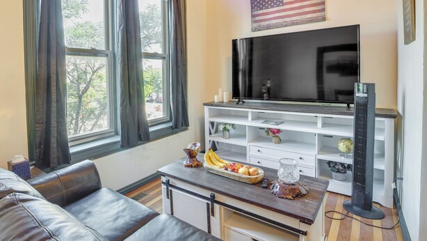 A living room with a leather sofa, a TV, a white entertainment unit, and a window with curtains. - Downtown Montrose Apartment, 12 Mi to Natl Park! (Montrose)