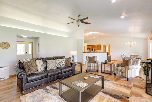 A living room with a dark brown leather sofa, a coffee table, and two armchairs. A ceiling fan is visible above the sofa.