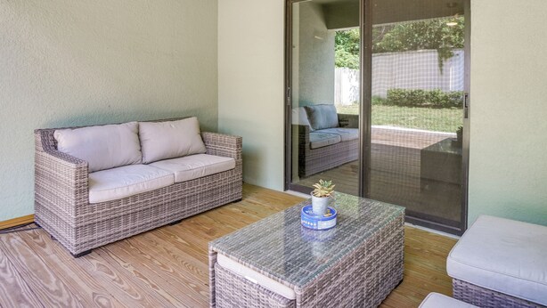 A wicker sofa with cushions, a glass-top coffee table with a decorative item, and a sliding glass door leading to an outdoor area.