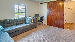 A living room with a gray sectional sofa, a black office chair, a wooden sliding door, and a window with blinds.