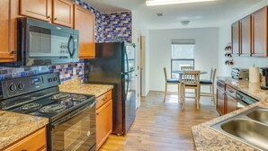 A kitchen with wooden cabinets, a stainless steel refrigerator, a black microwave, a stove, and a granite countertop.
