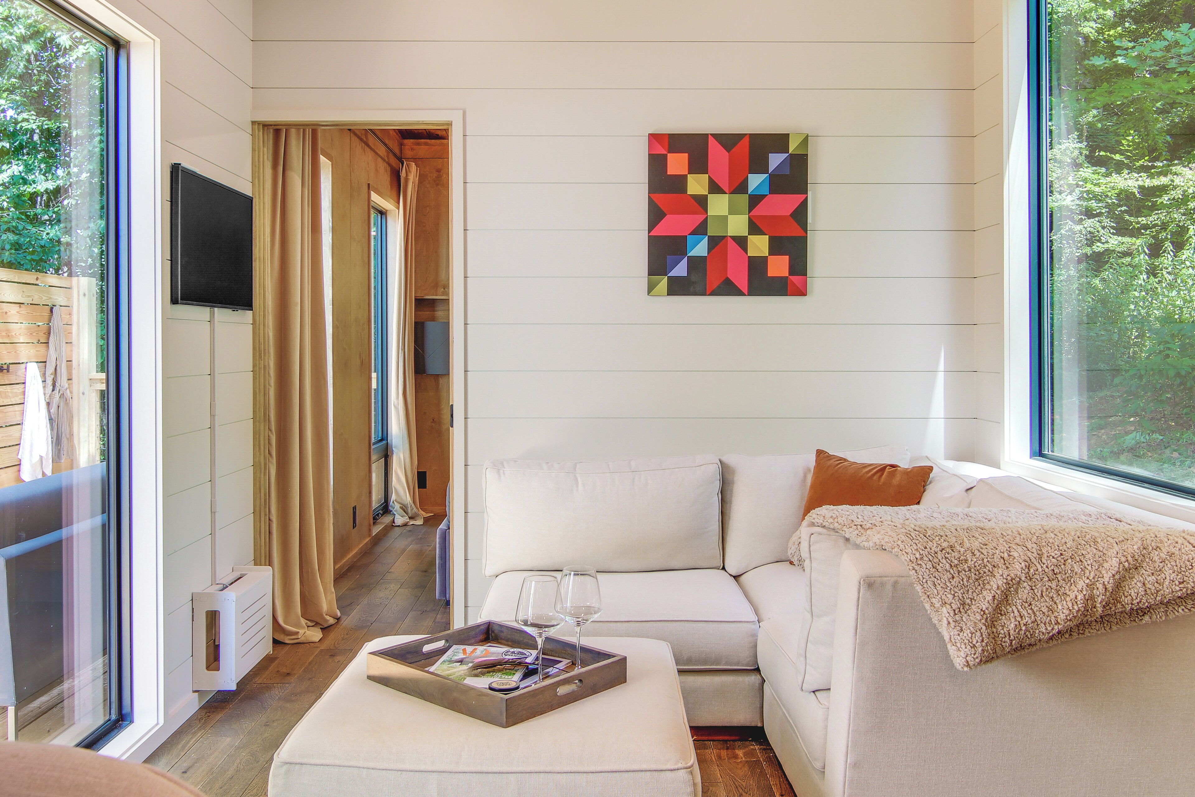 A modern living room with a white sofa, a coffee table with a tray and glasses, and a colorful geometric wall art piece.