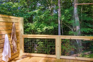 A wooden deck with a metal railing, a towel hanging on the wall, and a view of a forested area.