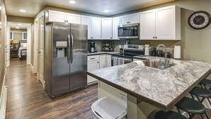 A modern kitchen with white cabinets, stainless steel appliances, a marble countertop, and a built-in trash can. - Laramie Gem < 1/2 Mi to University of Wyoming! (Laramie)