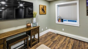 A room with a wooden desk, a mounted TV, a window with blinds, and a wall-mounted picture. - Laramie Gem < 1/2 Mi to University of Wyoming! (Laramie)