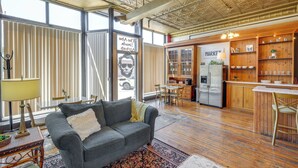 A spacious living area with a grey sofa, wooden flooring, and large windows. - Cozy Abode in Historic Yankton - Heart of the City (Yankton)
