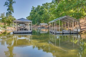 A tranquil lakeside setting with two covered docks, one with a gazebo and the other with a simple shelter, surrounded by lush greenery.