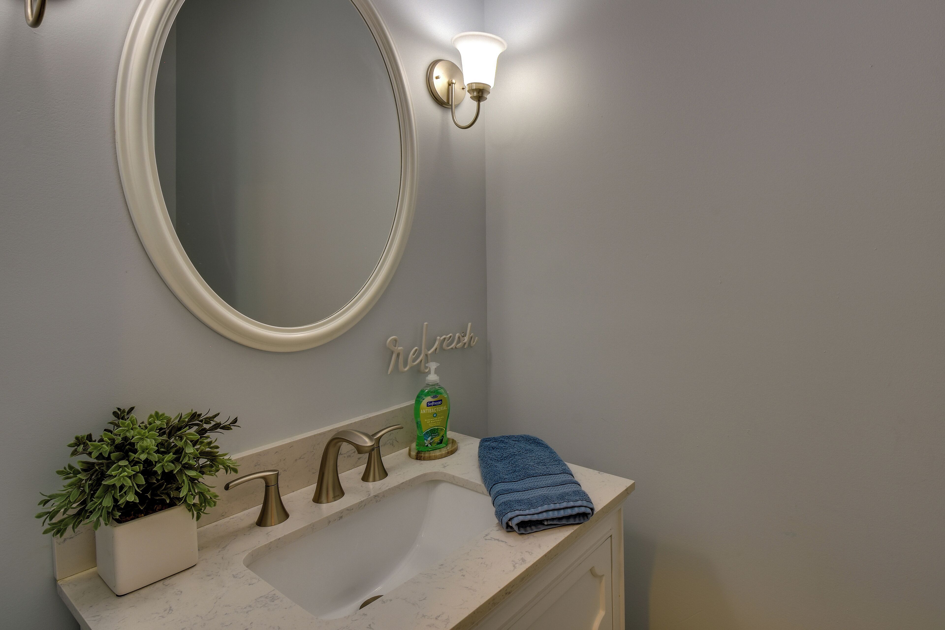 A bathroom with a round mirror, a light fixture, a sink, a plant, and a towel.