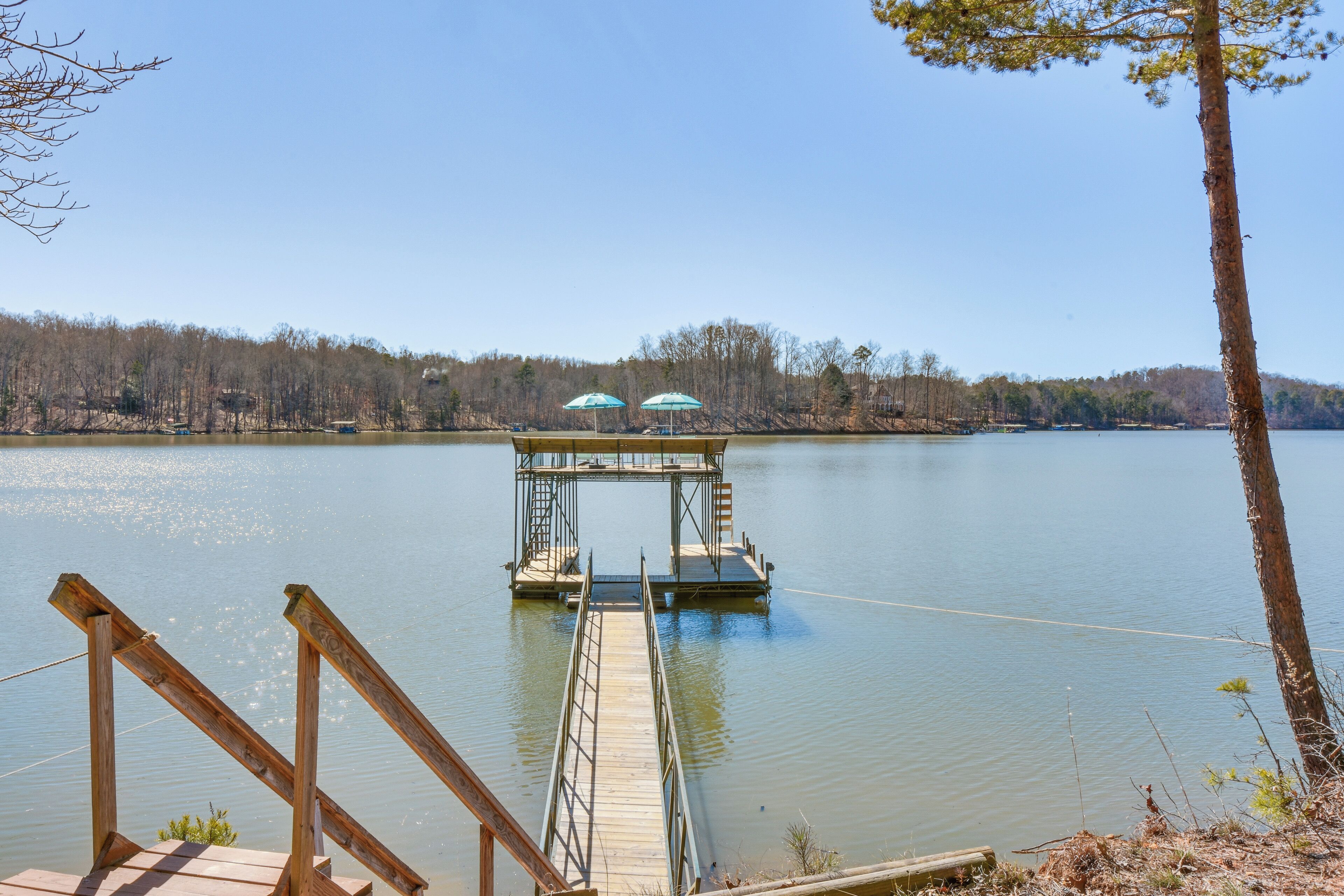 A wooden dock extending into a calm lake, with a small platform and two umbrellas.