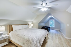 A bedroom with a large bed, a ceiling fan, a nightstand, a window, and a dark-colored sofa.