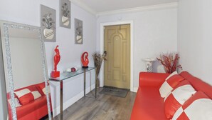 Een woonkamer met een rode bank, een glazen salontafel en een deur met een deurmat.