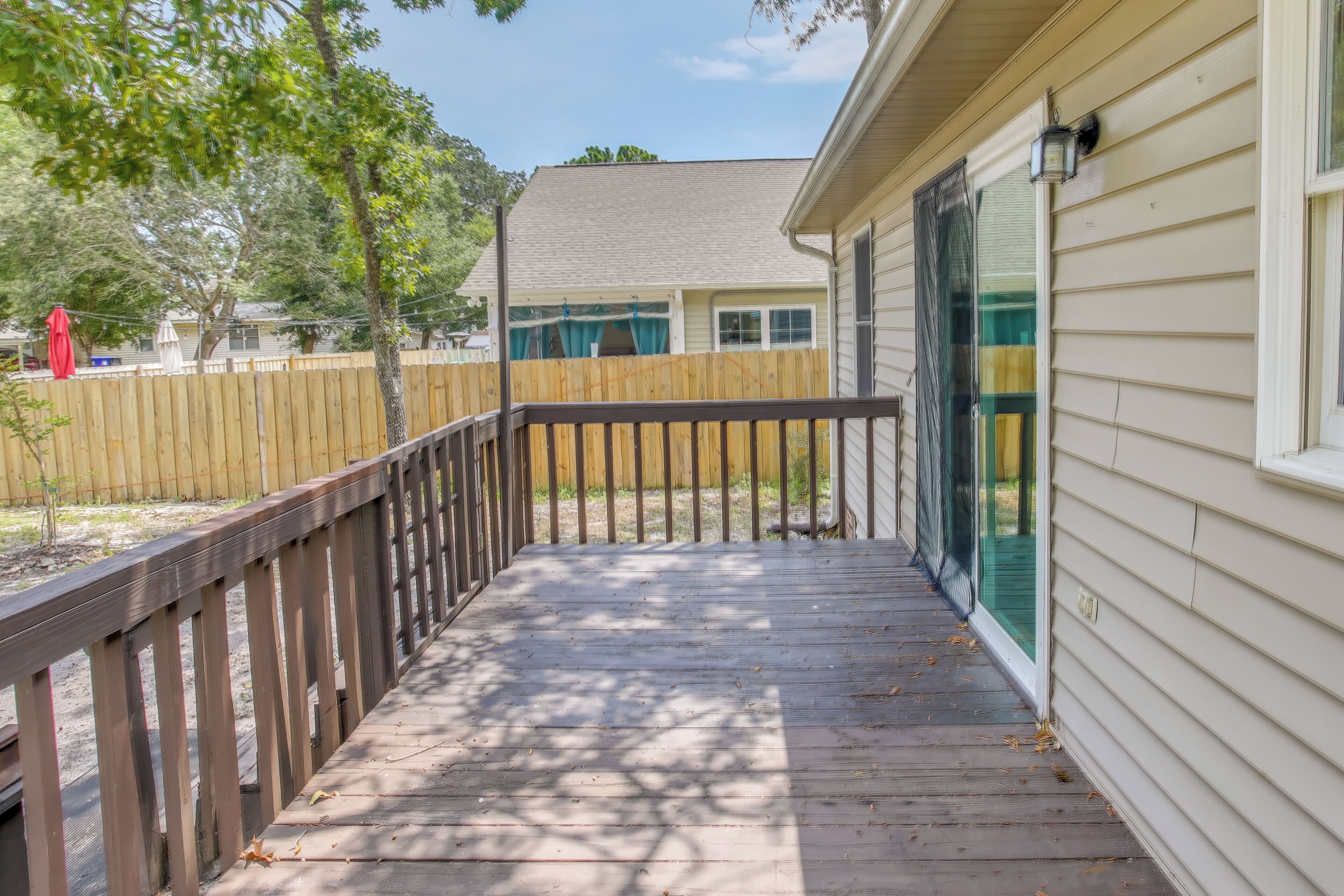 A wooden deck with a railing, leading to a house with a screened porch.