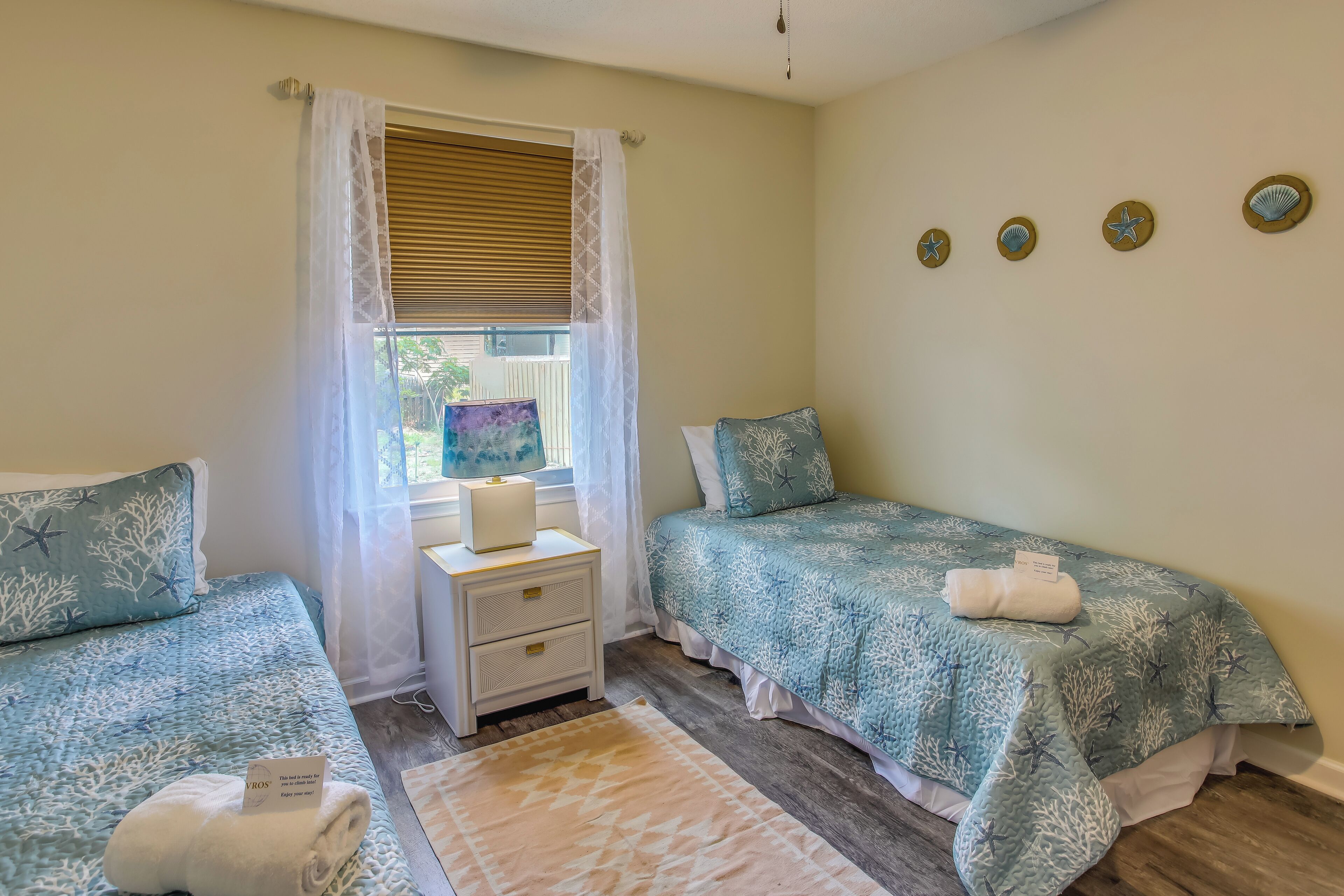 Une chambre avec deux lits, une table de chevet, une fenêtre avec des rideaux et des éléments de décoration murale.