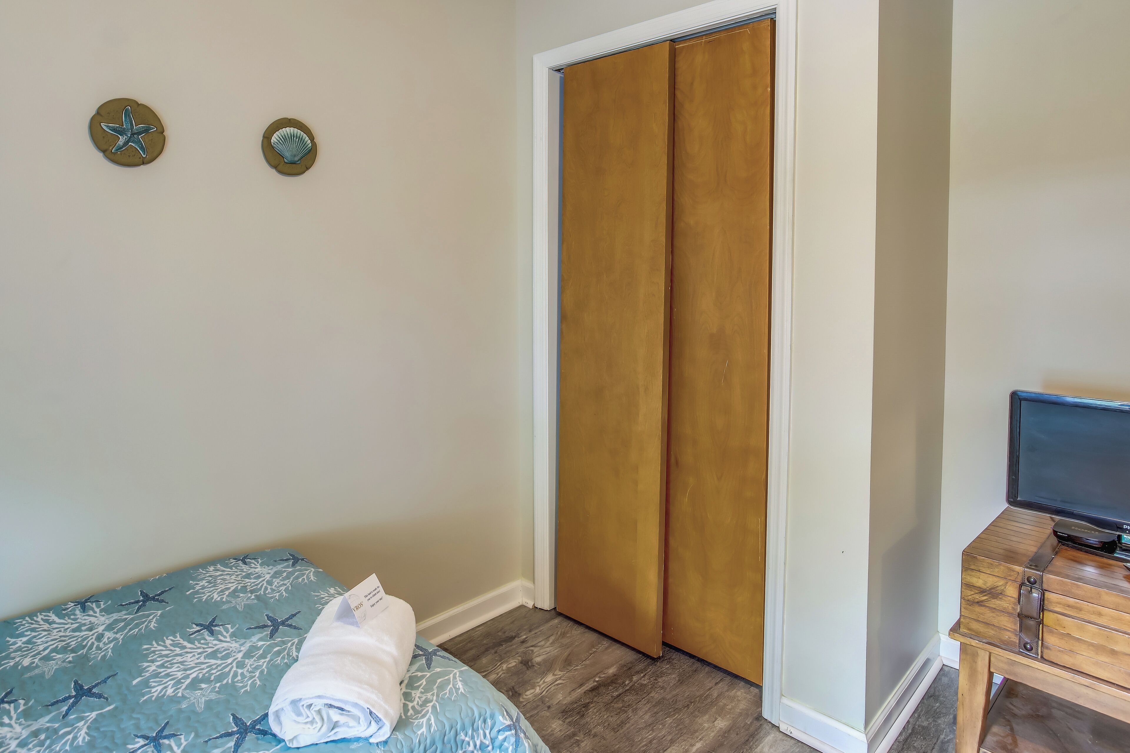 A bedroom with a bed, a wooden wardrobe, a small table with a television, and two wall decorations.