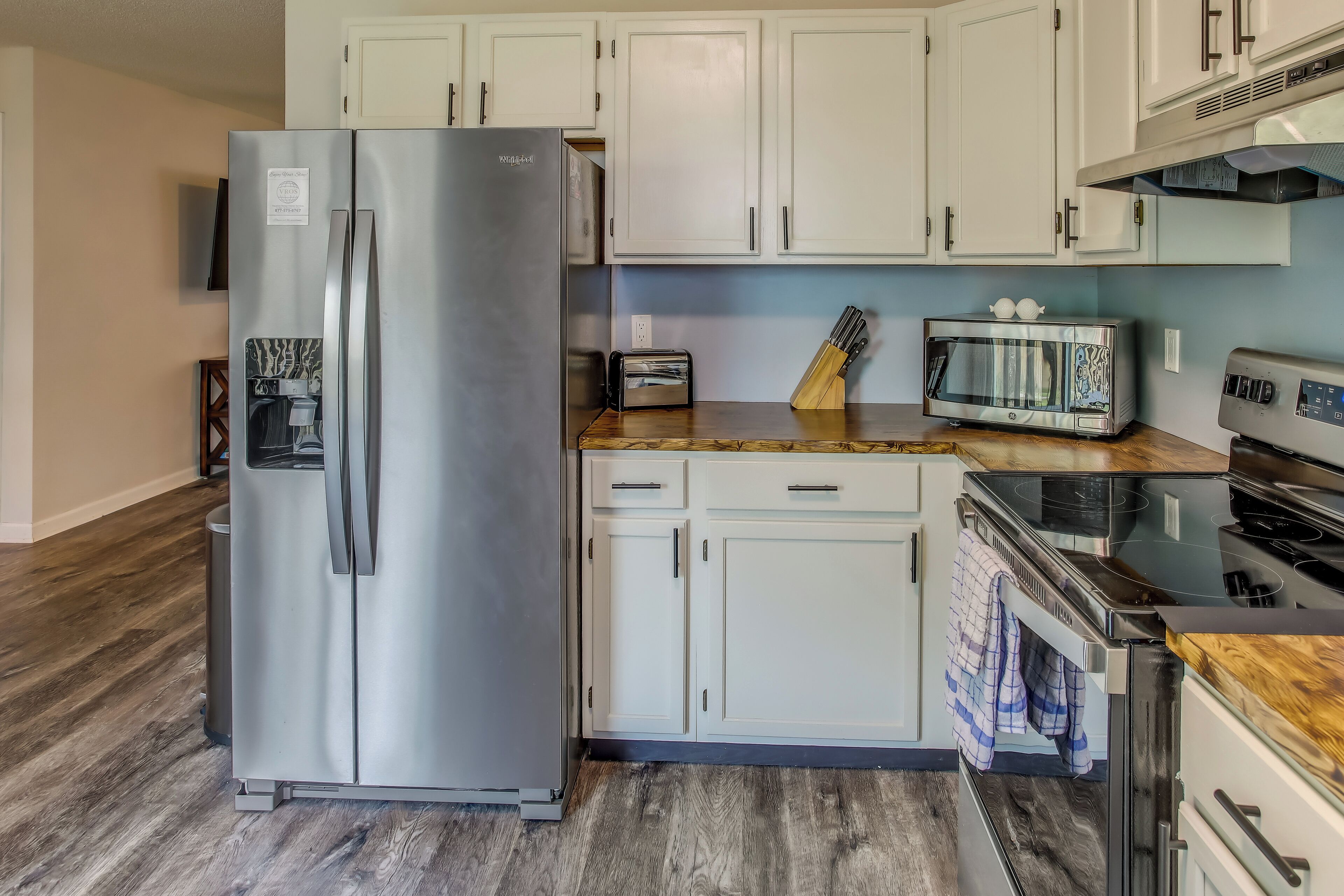 A kitchen with a stainless steel refrigerator, white cabinets, a microwave, a toaster, and a wooden countertop.