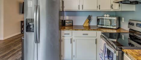 A kitchen with a stainless steel refrigerator, white cabinets, a microwave, a toaster, and a wooden countertop.