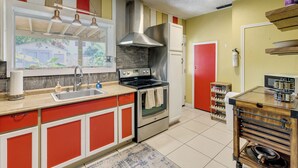 Una cocina con estufa de acero inoxidable, un lavamanos y una ventana con vista a una casa.