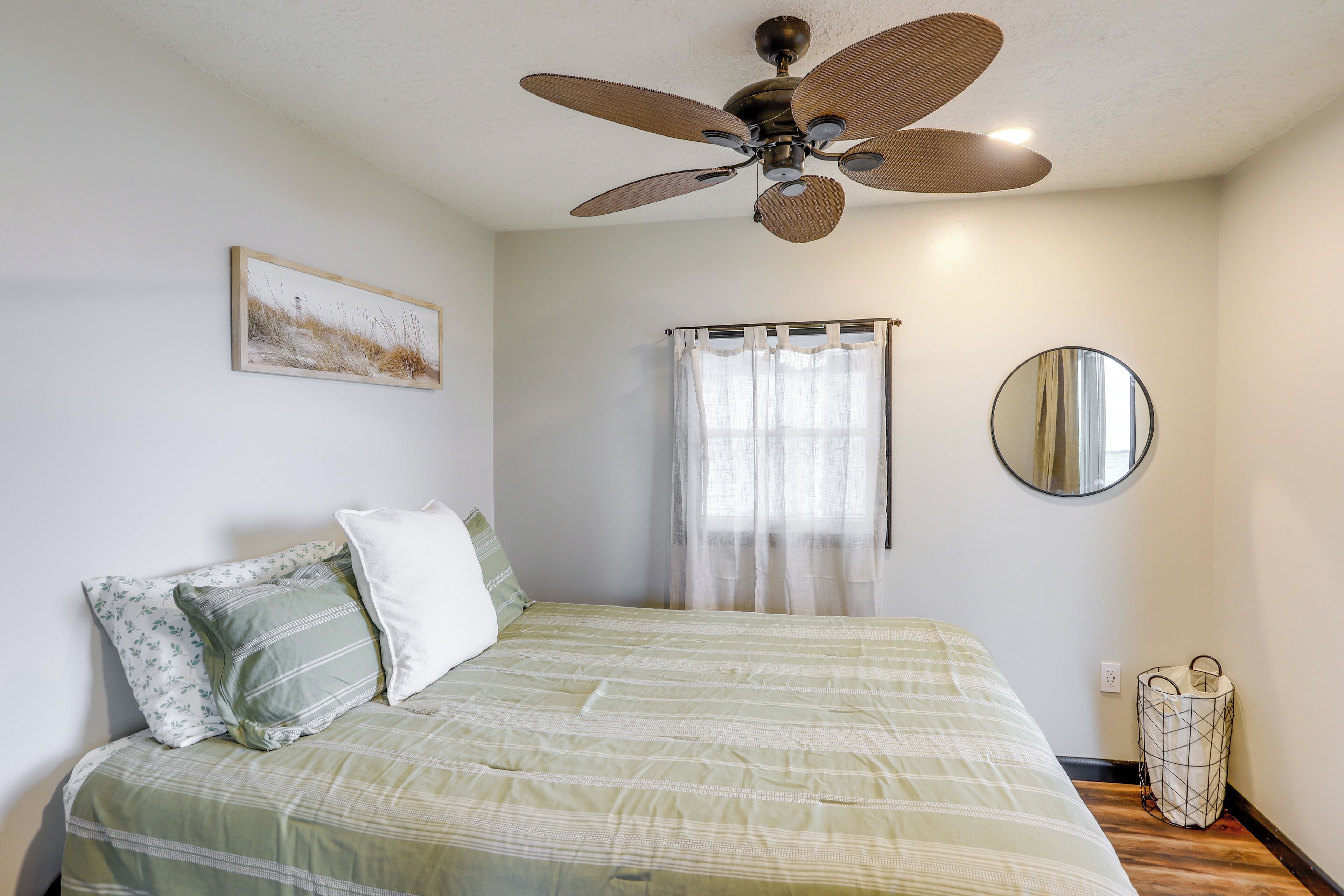 A bedroom with a bed, a ceiling fan, a window with curtains, a mirror, and a wall-mounted light switch.