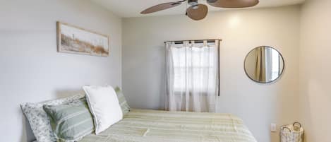 A bedroom with a bed, a ceiling fan, a window with curtains, a mirror, and a wall-mounted light switch.