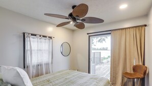 Un dormitorio con cama, ventilador de techo, ventana con cortinas y una silla.