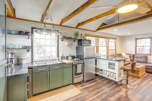 Een keuken met groene kasten, een roestvrijstalen koelkast en een magnetron. Er is een houten plafond en een raam met uitzicht op het landschap.