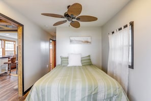Een slaapkamer met een bed, een plafondventilator, een raam met gordijnen en een schilderij aan de muur.