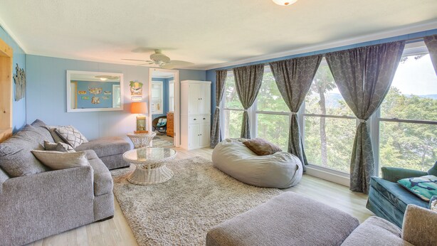 A living room with a sectional sofa, a bean bag, a glass coffee table, and a view of the outdoors through large windows. - Bright Byrdstown Home w/ Views of Dale Hollow Lake (Byrdstown)