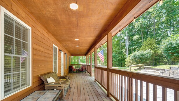 A wooden deck with a table and chairs, a bench, and a view of a forested area.