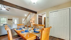 A dining area with a wooden table set for four, surrounded by wooden chairs. A staircase is visible in the background leading to another room.