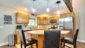 A kitchen with wooden cabinets, a stainless steel refrigerator, and a central island with two chairs.