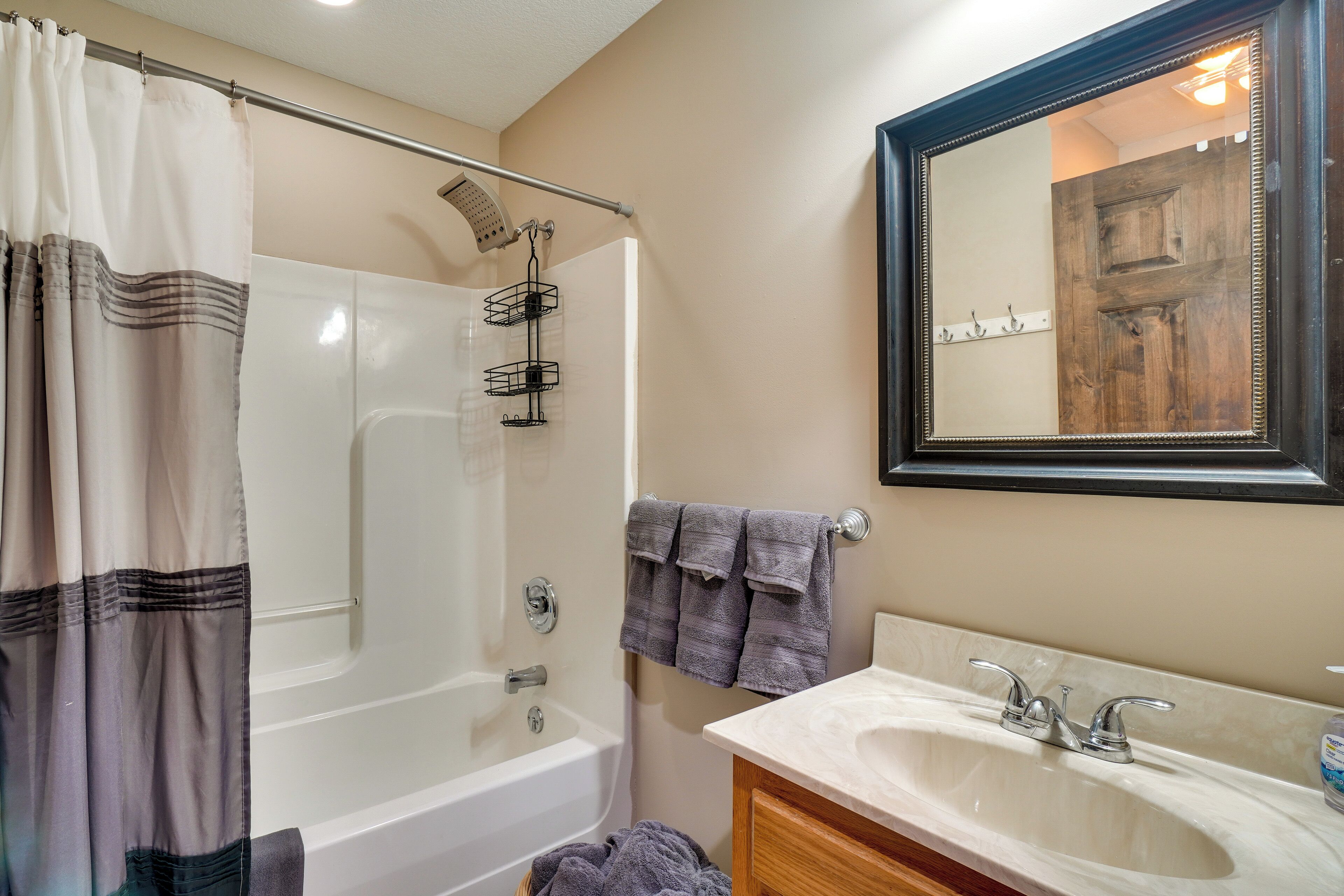 A bathroom with a bathtub, shower, vanity with a sink, and a mirror.