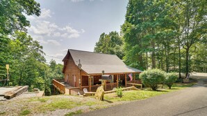 A log cabin with a porch, surrounded by trees and a gravel driveway.
