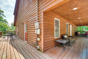 A wooden deck with outdoor furniture, a covered area with a table and chairs, and a window with a view of greenery. - Cozy Tennessee Lake House w/ Grill & Fire Pit! (Byrdstown)