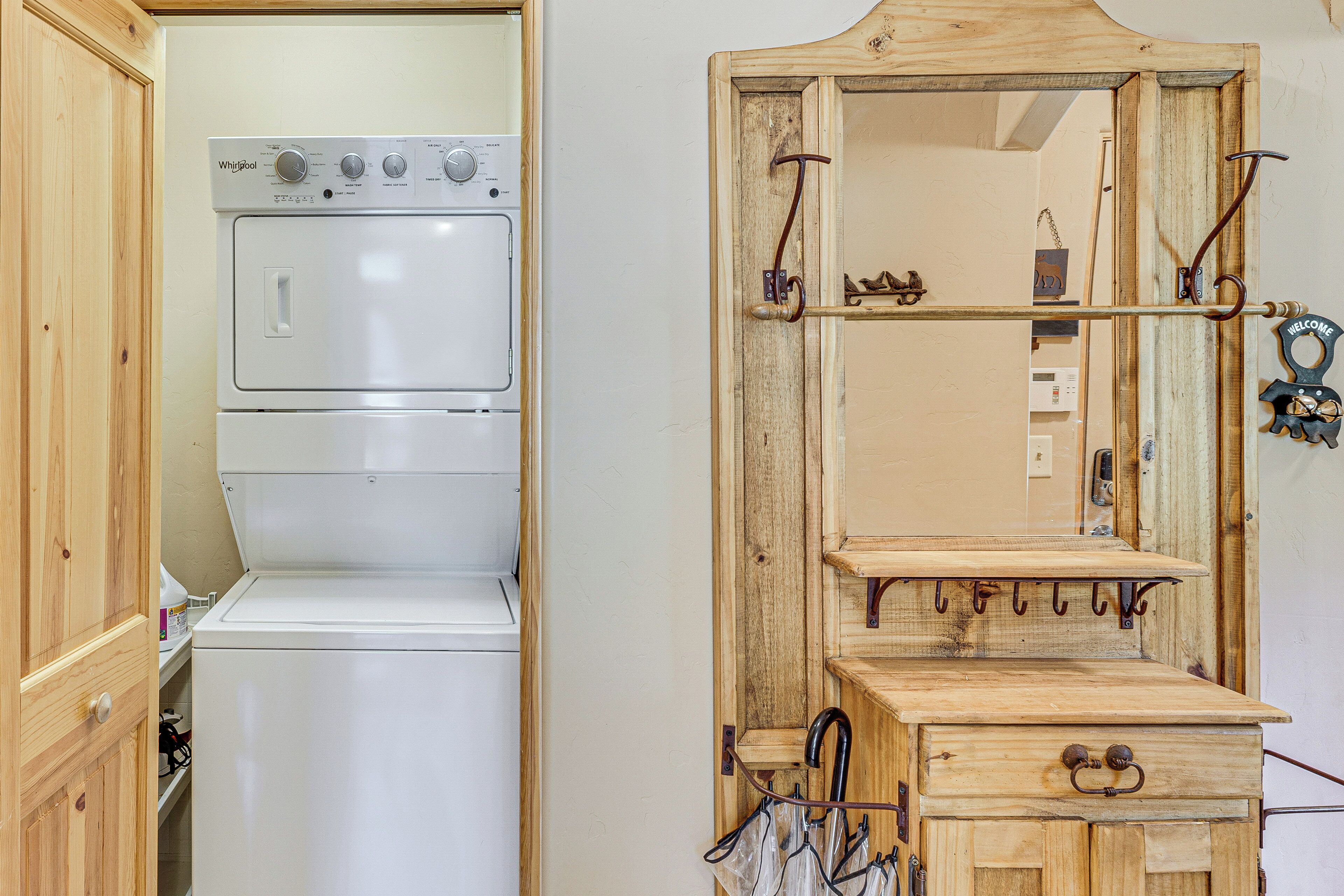 Ein Waschraum mit einer gestapelten Waschmaschine und einem Trockner, einem Holzschrank und einem Spiegel mit einem 'Welcome'-Schild.
