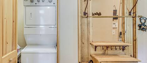 Ein Waschraum mit einer gestapelten Waschmaschine und einem Trockner, einem Holzschrank und einem Spiegel mit einem 'Welcome'-Schild.