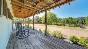A covered outdoor area with wooden flooring, a rocking chair, and a fenced riding arena in the background. - Secluded Blanco Home w/ Private River Access! (Blanco)