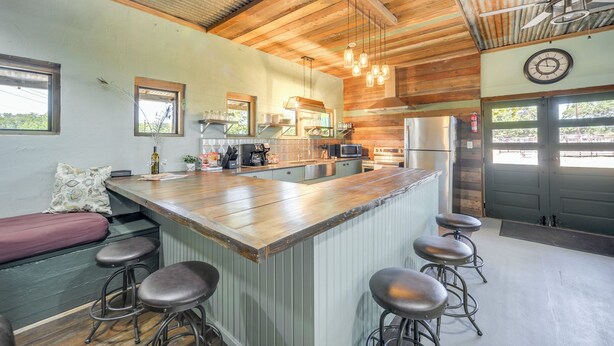 A kitchen with a wooden island, bar stools, a bench, and a view of the outside. - Secluded Blanco Home w/ Private River Access! (Blanco)